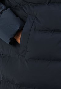 Navy blue puffer jacket with a textured, quilted design. Features a side pocket and contrasting material accents. Soft, smooth fabric.