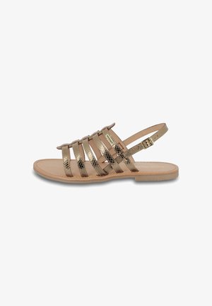 Sandale plate pour femme avec des brides texturées dorées métalliques et une boucle de cheville ajustable sur une semelle beige.