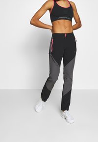 Black and gray athletic pants with pink zipper accents and logo on the side. Features a slim fit design and two front pockets.