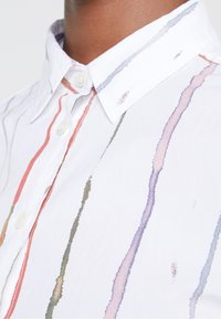 Witte button-up shirt met verticale aquarelstrepen in rood, groen en blauw. De stof lijkt soepel met een scherpe kraag.