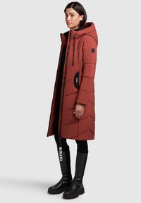 Raudonas, siuvinėtas pūkinis paltas su kapišonu, priekyje su užtrauktuku ir juodomis kišenėmis. Derinamas su juodais, storakulniais aukštakulniais iki kelio aulais.