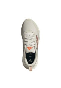 Zapatilla deportiva beige claro con tejido texturizado, acentos naranjas y suela acolchada. Presenta cordones y una plantilla negra con una marca.