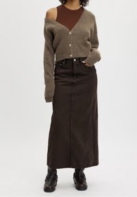 Brun korttröja med knappar, tillsammans med en brun denim maxikjol. Modellen bär svarta ankelstövlar med spännen.