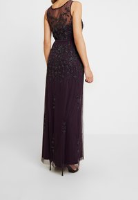 Sleeveless dark purple evening gown with floral bead embroidery and sheer back panel, worn with black high-heeled sandals.