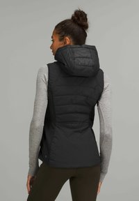 Gilet imbottito nero con collo alto e cappuccio, caratterizzato da una texture trapuntata e maniche lunghe grigie sottostanti. Vista posteriore che mostra un design slim fit.
