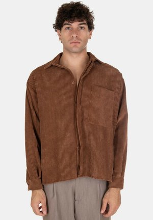 Camicia in velluto a coste marrone con bottoni frontali, una singola tasca sul petto e maniche lunghe, caratterizzata da una texture a coste e una vestibilità rilassata.
