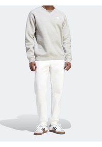 Šedá mikina s kulatým výstřihem a žebrovanými manžetami. V kombinaci s bílými kalhotami a klasickými teniskami s černými pruhy. Plochý stín dole.