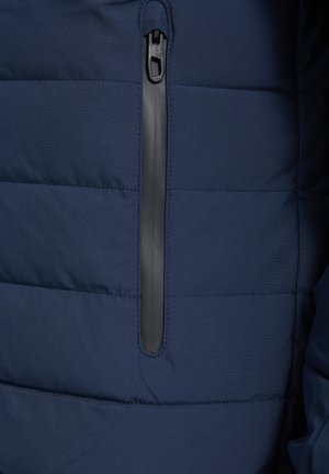 Navy blue quilted fabric with vertical black waterproof zipper pocket centered in the image on a jacket.