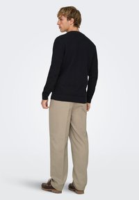 Pull noir en maille avec poignets et ourlet côtelés, associé à un pantalon beige clair et des chaussures marron, vu de dos.