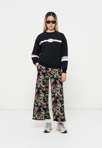 Sudadera negra con el logo de Roxy, combinada con pantalones anchos de flores que presentan hojas verdes y flores moradas. Zapatillas grises completan el conjunto.