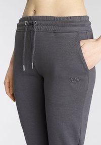Graue Jogginghose mit elastischem Bund, Kordelzug und Seitentaschen; verfügt über ein gesticktes "H.I.S"-Logo auf der linken Seite. Weiche Stoffstruktur.