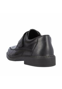 Chaussure en cuir noir avec une texture lisse, un bout rond et un petit talon. Une bride Velcro et des détails de couture rehaussent le design.