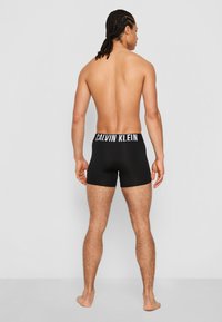 Black cotton boxer briefs with an elastic waistband featuring "CALVIN KLEIN" logo in white, fitted design showcasing the back view.