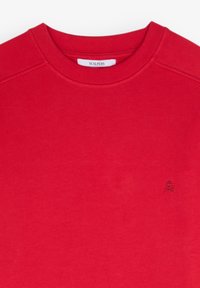 Sweat-shirt rouge col rond avec un petit logo brodé foncé sur la poitrine et une étiquette Scalpers à l'intérieur du col.