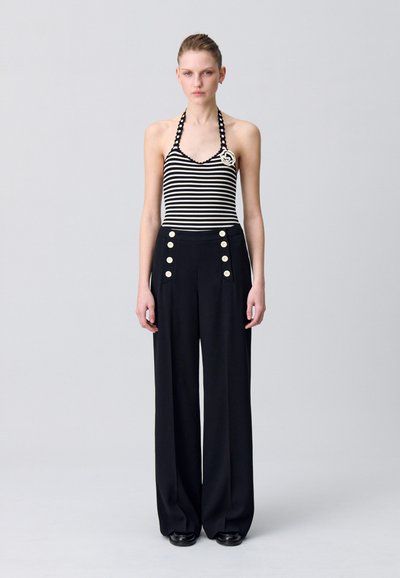 Top a fascia a righe con scollatura halter e bordi in pizzo abbinato a pantaloni neri a vita alta con bottoni dorati e vestibilità ampia.