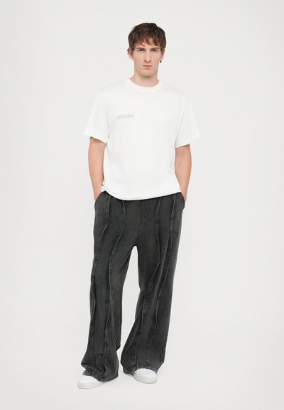 T-shirt en coton blanc avec un petit graphique sur la poitrine, associé à un pantalon en denim gris foncé à coupe ample avec des détails de couture incurvés.