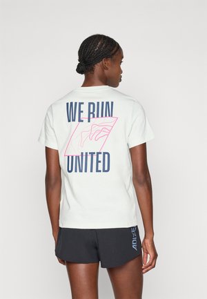 T-shirt en coton vert clair à manches courtes. Le dos présente "WE RUN UNITED" en bleu marine avec un design en contour rose. Texture lisse, coupe décontractée.