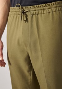 Joggers leggeri verde oliva con cintura elastica, cordoncino regolabile e tasche laterali, caratterizzati da un tessuto morbido e strutturato.
