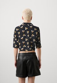 Camicetta nera a fiori con fiori bianchi e arancioni, maniche corte e colletto. Abbinata a pantaloni corti in pelle nera.