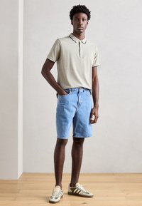 Cămașă polo de un verde deschis, cu guler contrastant, asortată cu pantaloni scurți din denim albastru și adidași verzi. Design simplu, croi lejer, fără modele.