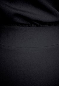 Czarna tkanina o gładkiej fakturze, z dopasowanym pasem i subtelnymi detalami szwu. Całość ma minimalistyczny i elegancki design.