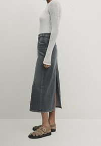 Jupe midi en denim gris avec fente latérale, associée à un haut à manches longues blanc et des sandales beiges avec un détail de boucle.
