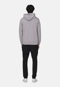 Sudadera gris con capucha ajustable y puños acanalados, combinada con pantalones negros. La tela parece suave, con un corte relajado. Se llevan zapatillas blancas.