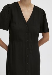 Vestido negro de botones con mangas cortas abullonadas, escote en V, tejido suave y una cintura ajustada que se transforma en una falda suelta.