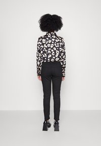 Dlouhá halenka s černobílým leopardím vzorem, spárovaná s úzkými černými kalhotami a masivními černými lodičkami na podpatku.