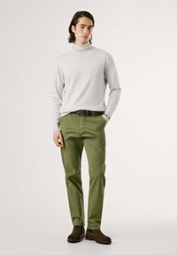 Maglione a collo alto grigio chiaro, pantaloni verde oliva, cintura marrone e stivali alla caviglia marroni scuri. Design semplice, texture liscia e vestibilità su misura.