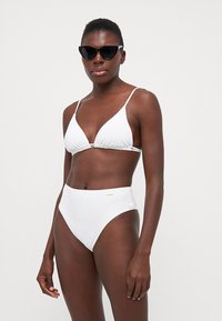 Completo bikini bianco con top triangolare e spalline sottili, e slip a vita alta, realizzato in tessuto morbido con una leggera lucentezza.