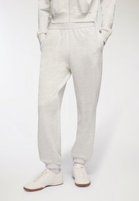 Jasnoszare dresy wykonane z miękkiego materiału, z elastycznym pasem, bocznymi kieszeniami i elastycznymi mankietami. Noszone z białymi sneakersami.