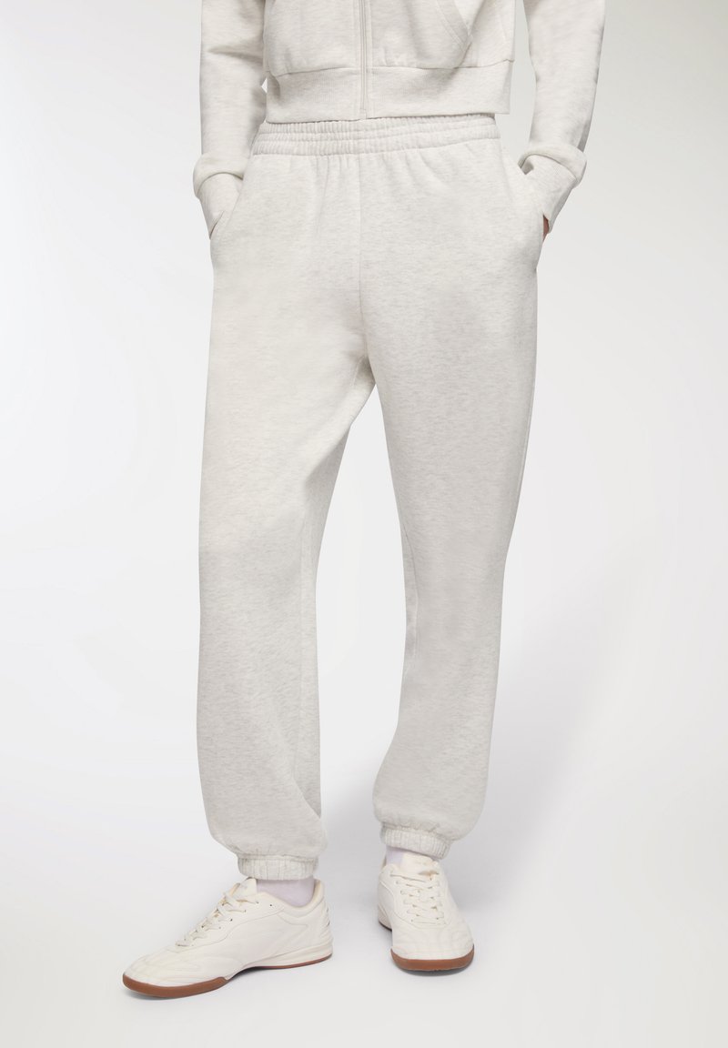 Jasnoszare dresy wykonane z miękkiego materiału, z elastycznym pasem, bocznymi kieszeniami i elastycznymi mankietami. Noszone z białymi sneakersami.