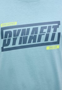 Μπλε ύφασμα με έντονο σκούρο μπλε κείμενο "DYNAFIT", κίτρινα σημεία με τις λέξεις "SKIMO EQUIPMENT" και "SINCE 1950" σε ορθογώνιο σχέδιο.