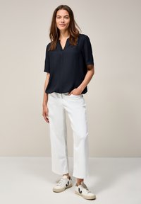 Blouse marine à manches courtes avec un col en V, associée à un pantalon large blanc et des baskets crème avec des accents noirs. Tissu lisse, coupe décontractée.