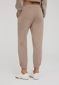 Pantaloni della tuta beige realizzati in tessuto morbido, con vita elastica, tasche laterali e polsini elastici alla caviglia. Indossati con sneaker bianche.