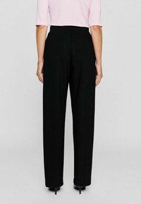 Zwarte high-waisted broek met een rechte pasvorm, gladde textuur en minimalistische stijl, gecombineerd met zwarte hakken.