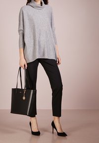 Jasnoszary sweter z golfem o luźnym kroju, czarne slim fit spodnie, czarna torba na ramię z metalowym akcentem oraz czarne czółenka na szpic.