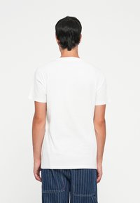 Tricou alb din bumbac, cu mâneci scurte, design cu gât rotund și croială lejeră. Spatele este simplu, fără logo-uri sau modele.