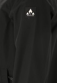 Svart jacka med en slät yta, med en framträdande vit "Whistler" logotyp patch i en bergdesign på ärmen.