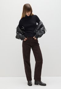 Schwarzer gerippter Rollkragenpullover, übergroße schwarze Bomberjacke, braune Leopardmuster-Hosen und schwarze Stiefeletten mit Blockabsatz.