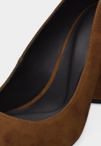 Κοντινό πλάνο καφέ γούνινου παπουτσιού με ψηλό τακούνι, μαύρο μαξιλαράκι στο εσωτερικό και στρογγυλή μύτη.