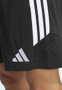 Μαύρα αθλητικά σορτς με τρεις κατακόρυφες λευκές ρίγες και ένα λευκό τρίγωνο λογότυπο που φοριέται στο μηρό ενός ατόμου.