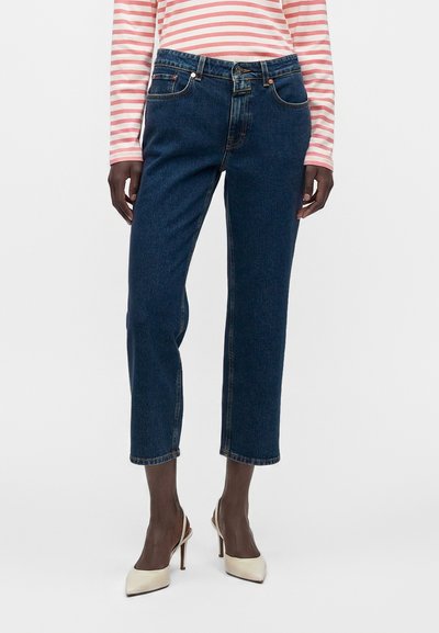 Personne portant un jean droit court bleu foncé, un haut à manches longues rayé rose et blanc, et des chaussures à talons beige.