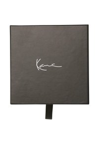 Melna taisnstūra kaste ar gludu tekstūru un magnētisku aizdari. Priekšpusē ir balta paraksta uzlīme un atvilktne atvēršanai.