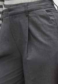 Σκούρο γκρι παντελόνι από υφασμάτινη υφή, με πιέτες, εφαρμοστή γραμμή και ζωνάκι με θηλιές για ζώνη.