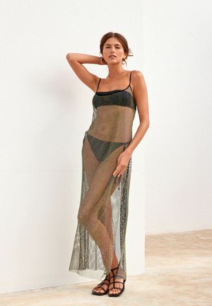 Schwarzes Mesh-Maxikleid mit dünnen Trägern, das ein durchsichtiges Design und Seitenschlitze aufweist. Getragen über schwarzem Badeanzug und kombiniert mit flachen, schmalen Sandalen.
