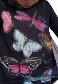 Svart tygtröja med färgglada fjärilstryck i rosa, grönt och orange, med handskriven text "I 88 YOU" och "I AM MY PASSIONS."