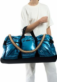 Blauwe puffer duffel tas met zwarte basis, met twee zijvakjes, overgrote handvatten en een oranje gevlochten band. Gladde, glanzende textuur.