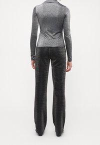 Glänzendes schwarzes und metallisches silbernes Langarm-Oberteil, kombiniert mit passenden, ausgestellten Hosen, die ein figurschmeichelndes Design und eine glatte Textur aufweisen.